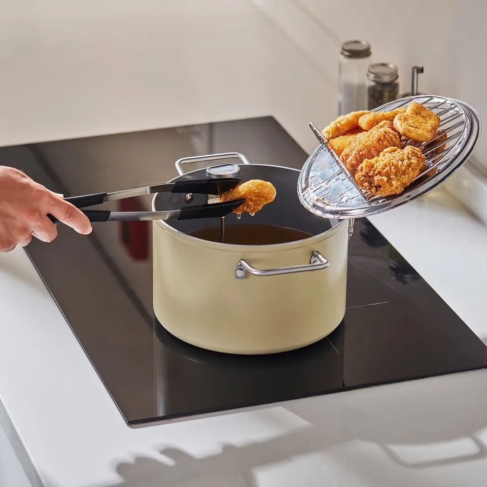 Hand uses tongs to chip food in pot; oil drains via rack.