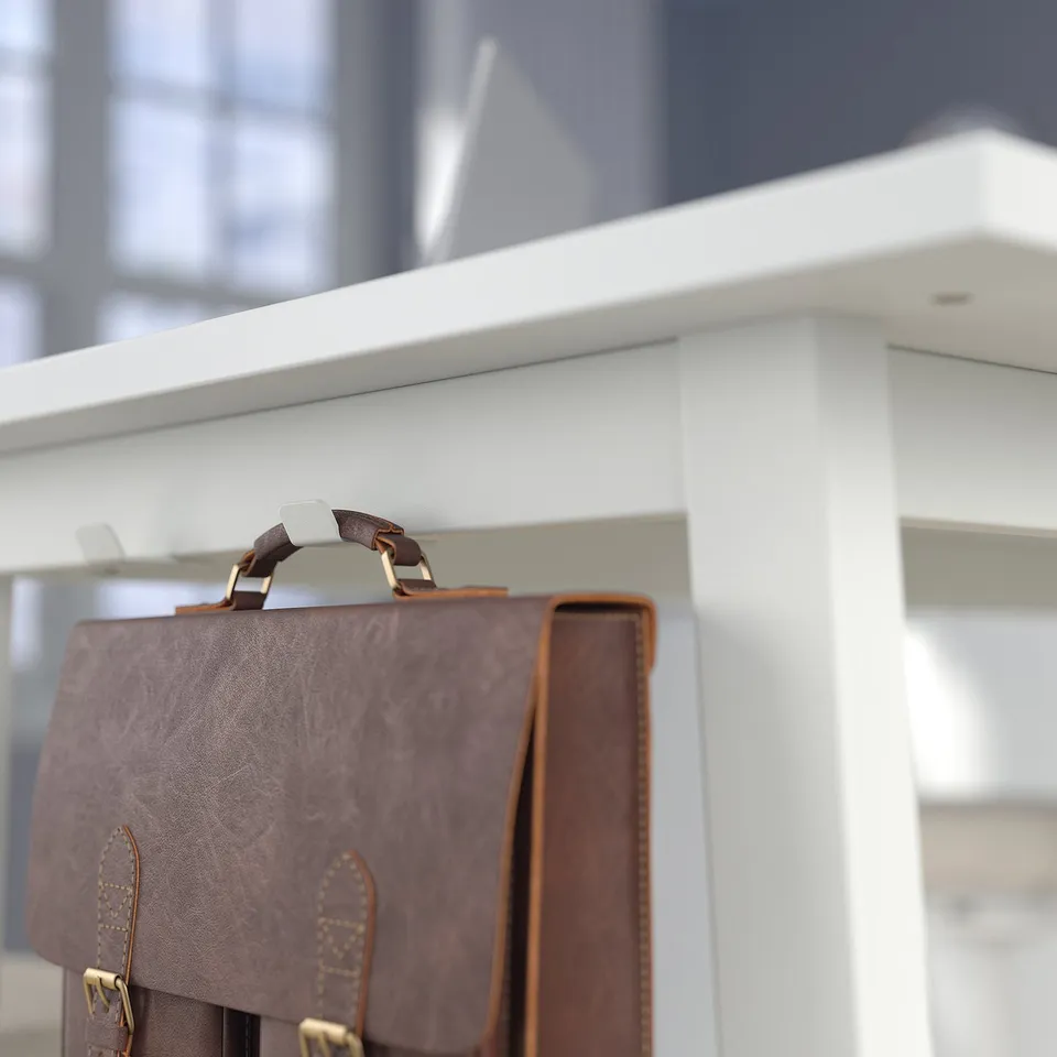 Brown leather bag hangs from metal hook on sleek, white conference table designed for sitting or standing meetings.
