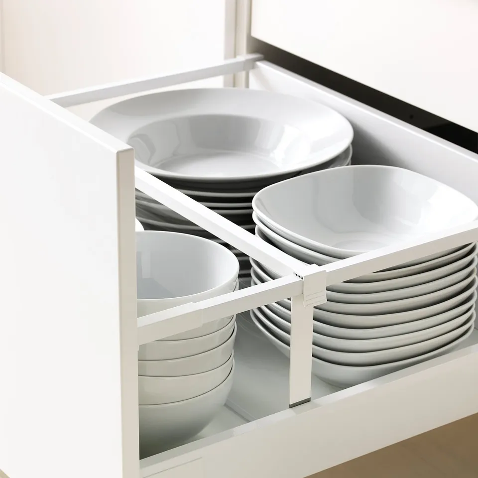 Open kitchen drawer showing organised stacks of white plates and bowls in compartments.