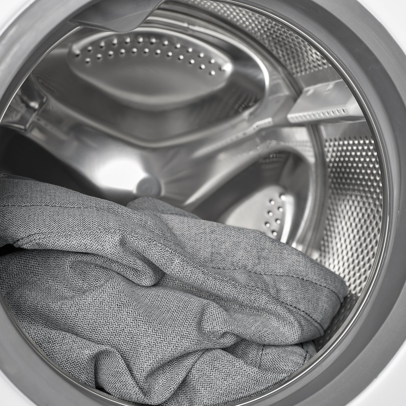 A washing machine drum with a grey fabric item inside. The drum has metallic perforated walls and a central agitator.