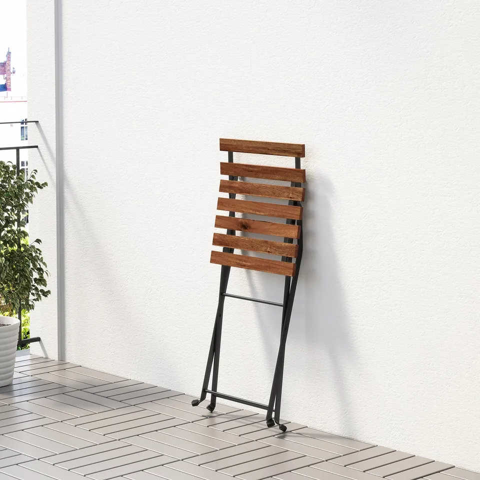 A wooden folding chair with metal legs. Its designed for easy storage and suitable for balconies, as seen against a white wall.