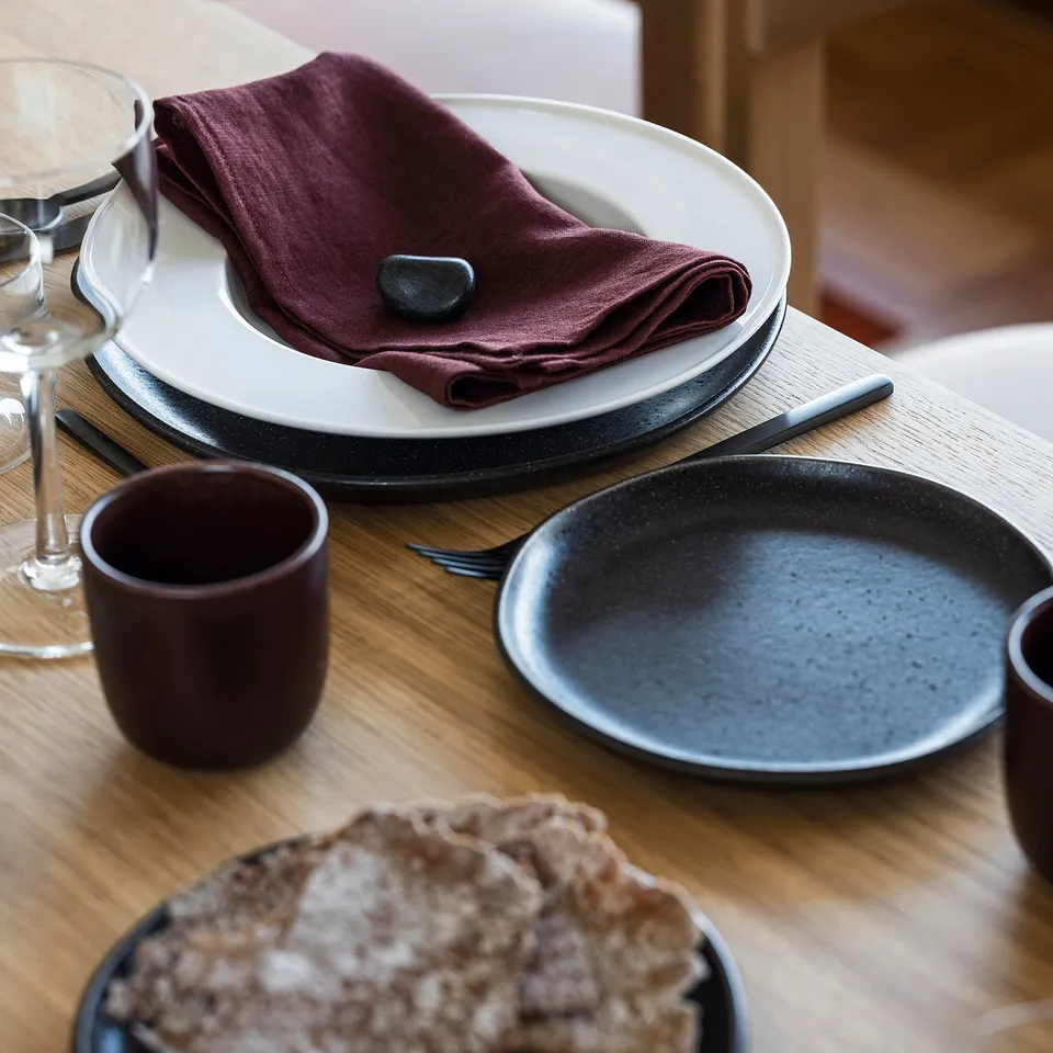 A table setting featuring a linen napkin, a plate, cup, and a dish, showcasing scandinavian design on a wooden table.