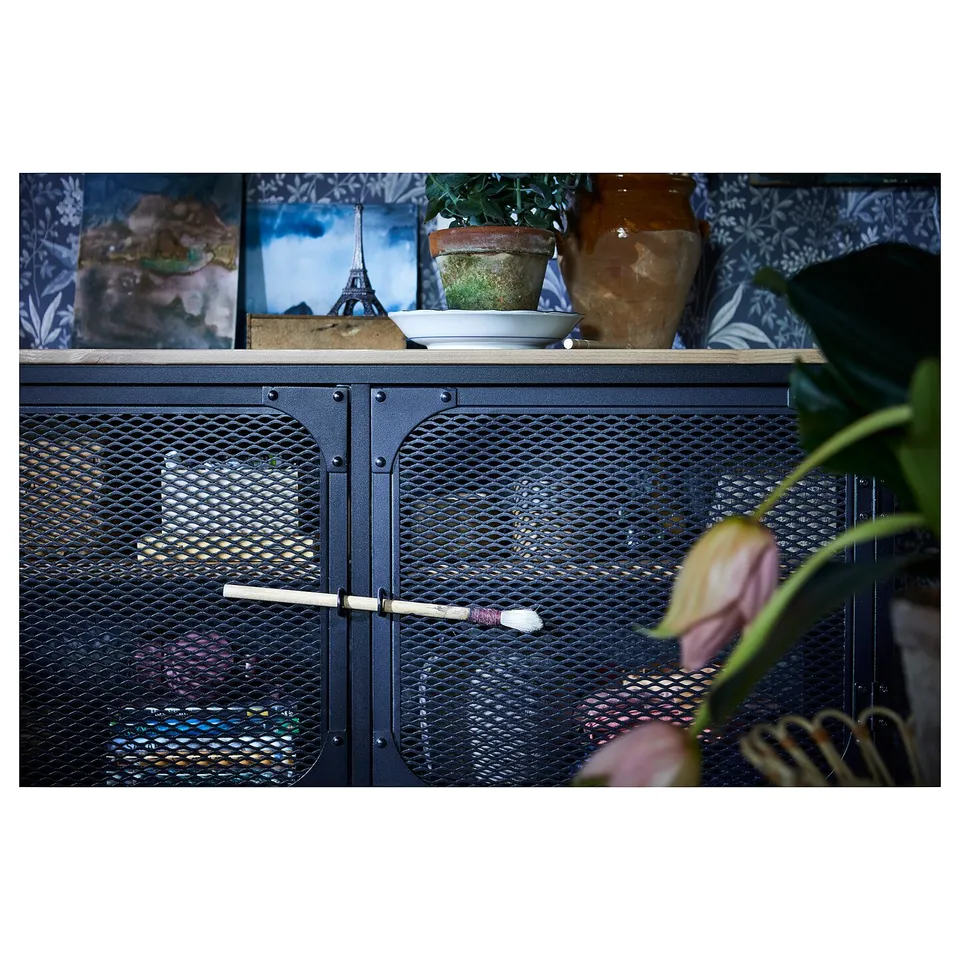 Industrial-style black metal and wood storage unit with mesh doors, displaying decorative items.