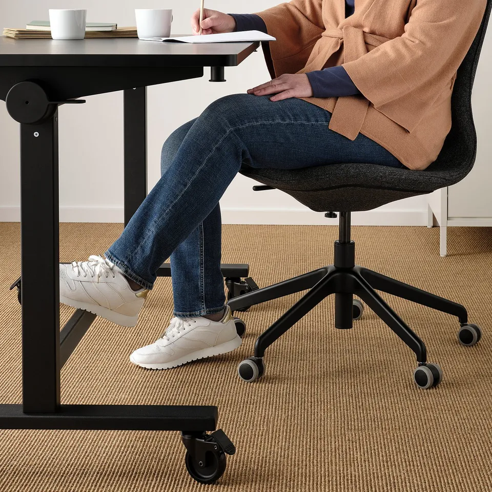 Person sitting at a height-adjustable desk with MITTZON footrest for leg support.