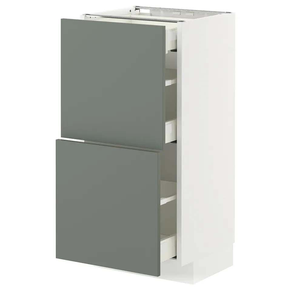 A modern kitchen cabinet from the METOD system with grey-green nickebo fronts. It has one drawer and one door, both partially open.