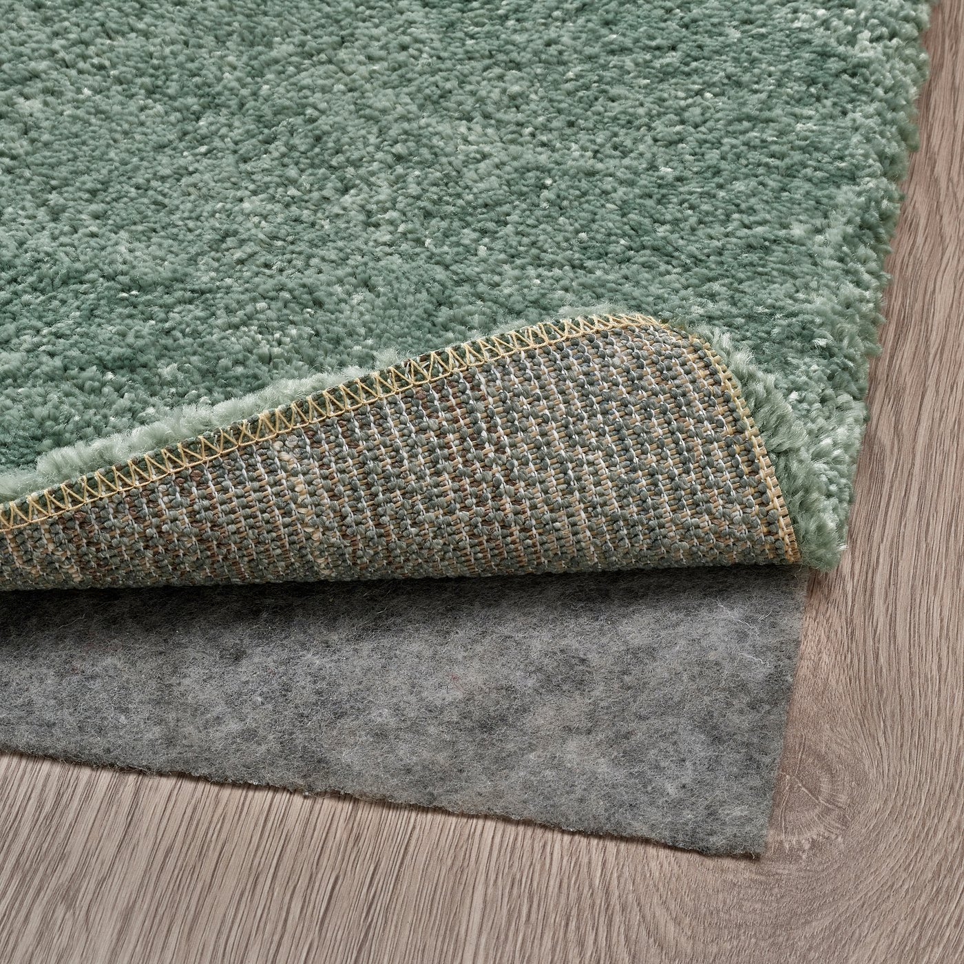 Green rug with thick pile, folded to show backing and non-slip underlay.