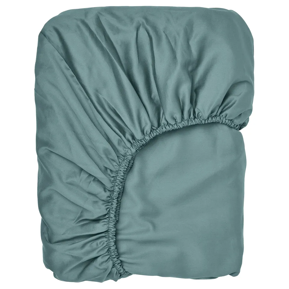 A teal blue-green fitted sheet, smooth and lustrous, folded neatly. Made of cotton and lyocell, designed to fit mattresses up to 26 cm thick.