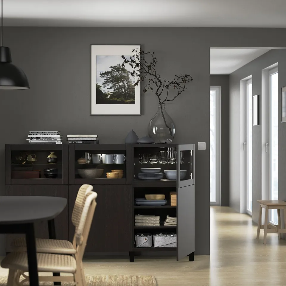 Modern dining area with dark wooden BESTÅ sideboard, storing dishes and decor. Glass doors and adjustable shelves
