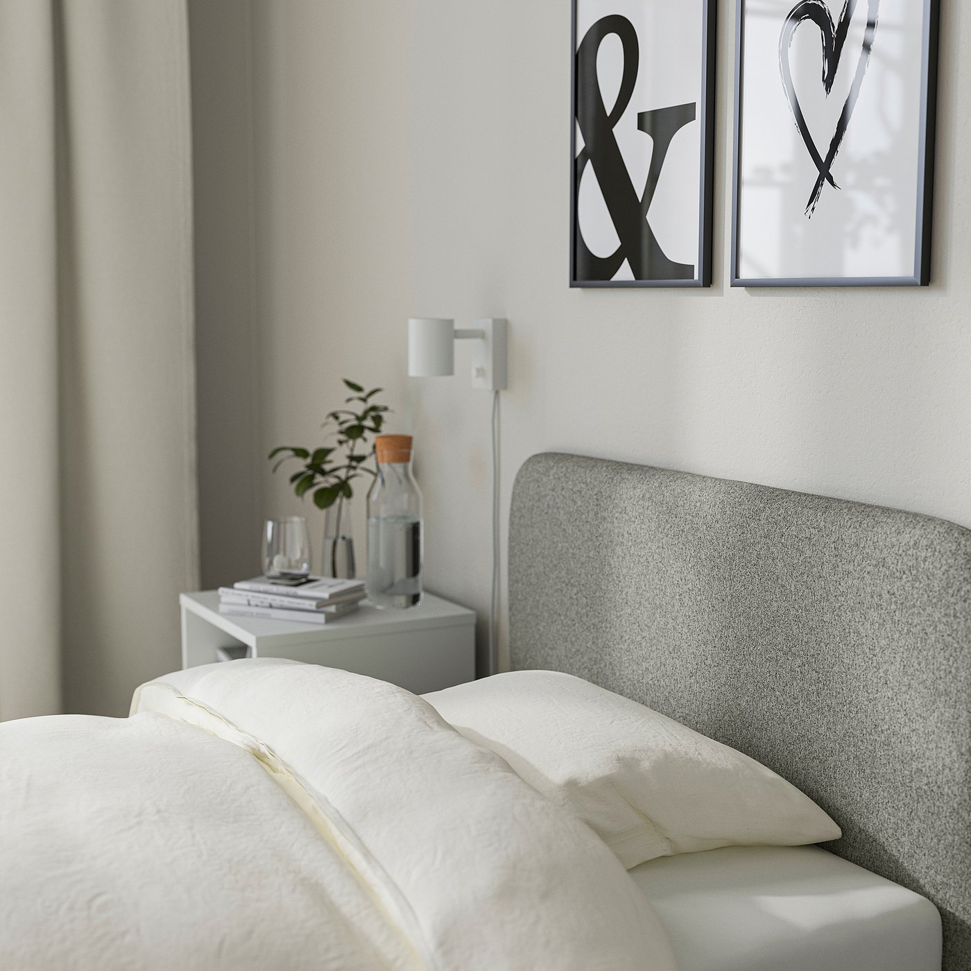 Modern bedroom with white bedding on a grey upholstered bed, featuring a headboard slipcover. Beside the bed is a bedside table with plants and books.