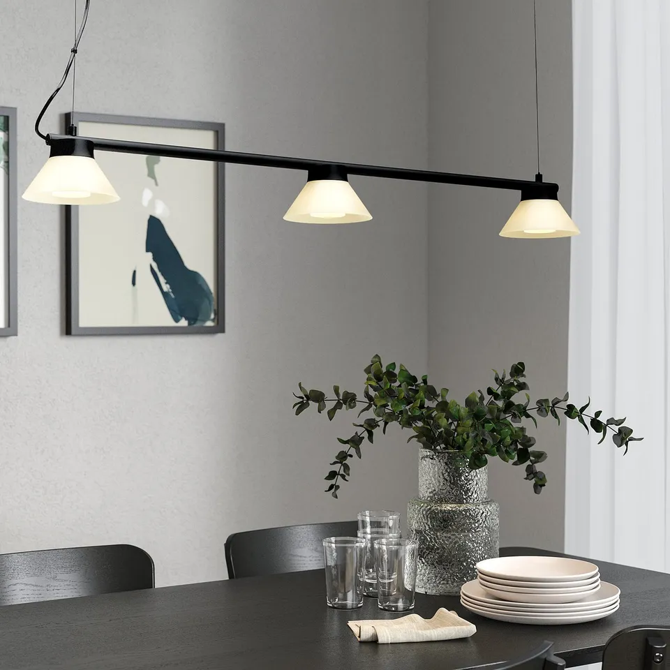 Modern dining area with SAMBORD lamp over table set with glasses, plates and greenery. Sleek, minimalist design with ample light.