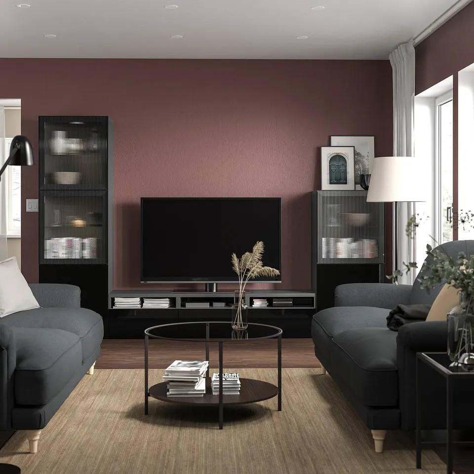 Modern living room with maroon walls, grey couches, tv stand with storage, glass coffee table, and plants.