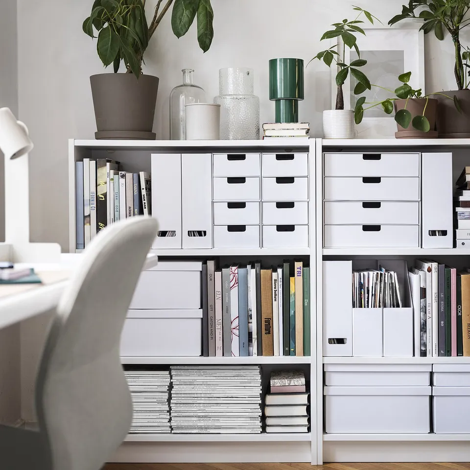 White bookshelf with organised books, papers, and decor. FJÄDERHARV magazine files blend well in minimalist design.