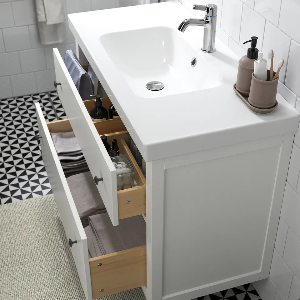 White bathroom vanity with open drawers revealing organised toiletries. Includes sink, tap, and storage compartments.