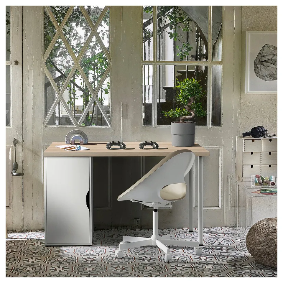 Home office with wooden desk, grey cabinet, white chair, large window, plant, office supplies, geometric print on textured wall, patterned rug.