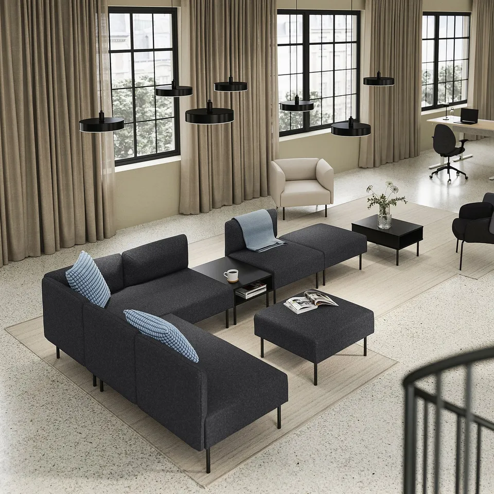 Modern office lounge with LILLEHEM dark grey sofa, black tables, beige chair, black pendant lights, and large windows.