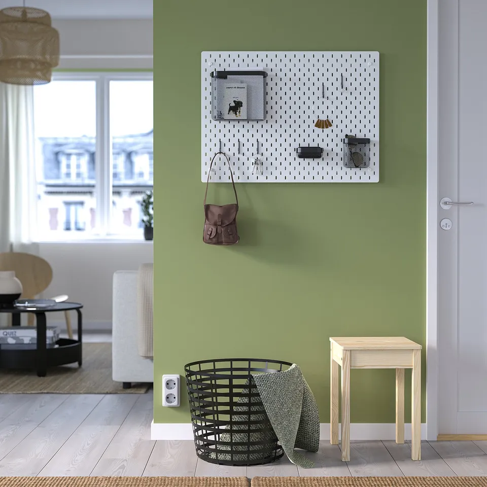 Green wall SKÅDIS pegboard with purse & items, black basket with towels, wooden stool, large windows.