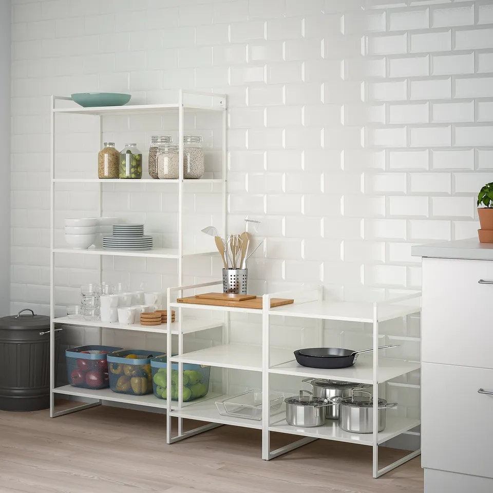 White JONAXEL shelving unit holds kitchenware, fruits, and pans. Steel, modern design, standard size next to cabinets.