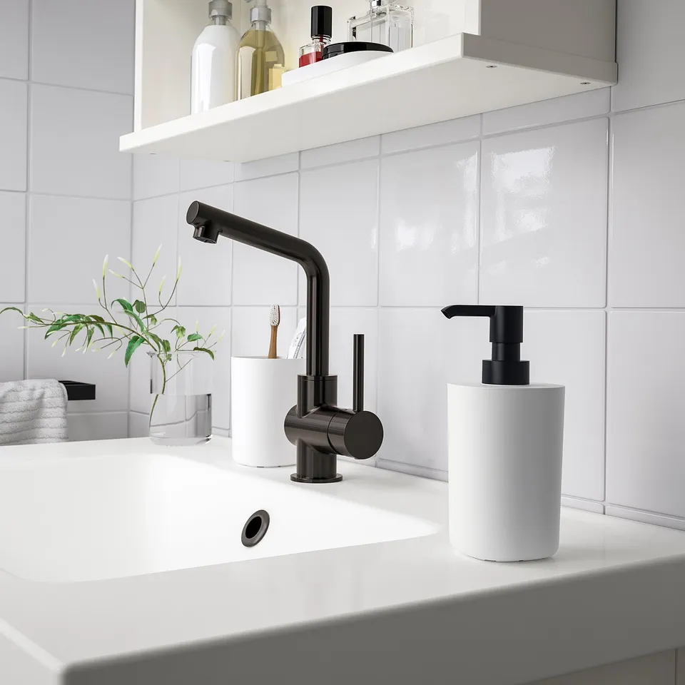 Modern bathroom: white sink, black tap, accessories. Black-detail soap dispenser, vase with greenery.