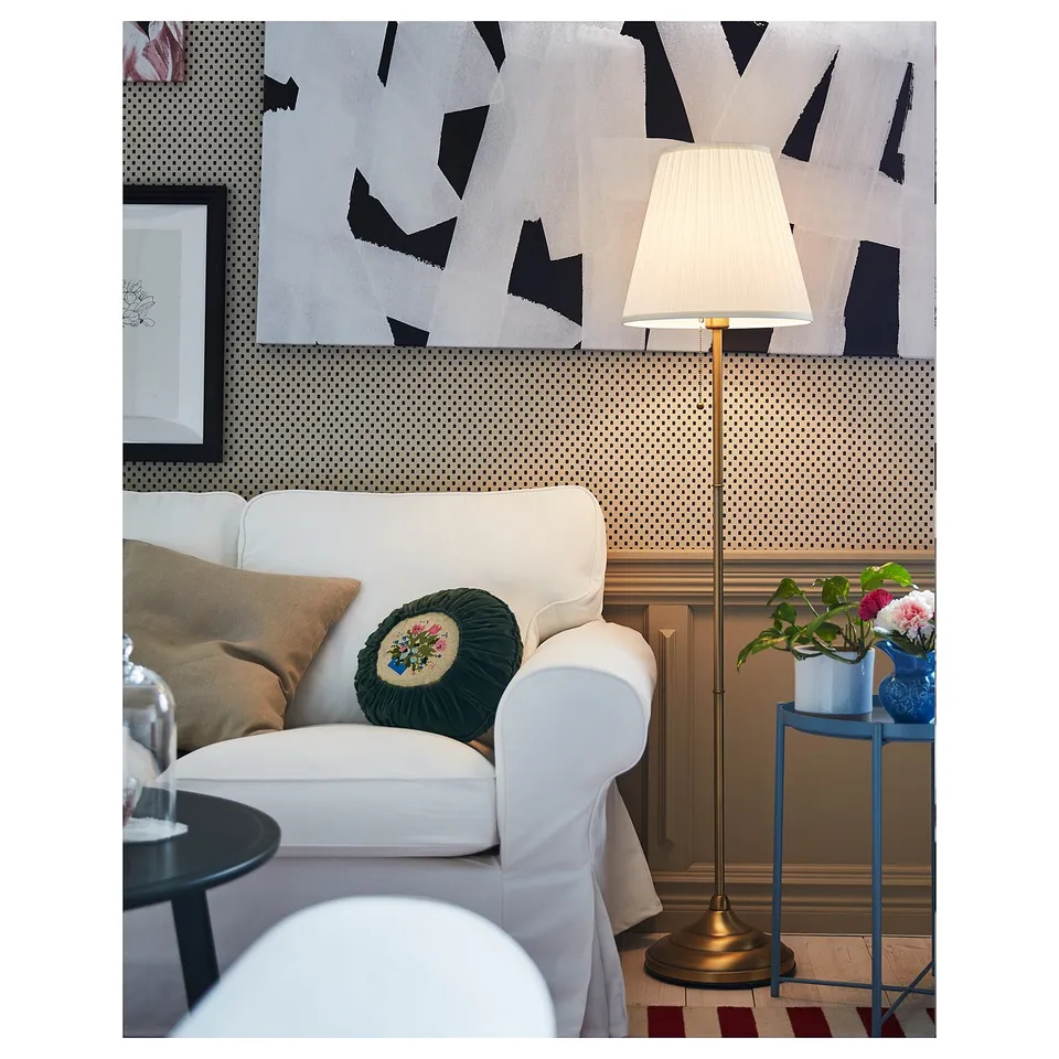 Modern living area with white armchair, patterned wallpaper, tall floor lamp with beige shade, and blue plant stand.