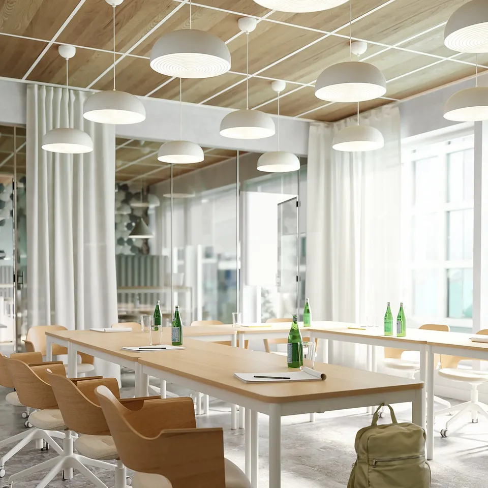 Modern office area with long tables and wooden chairs, green bottles, and hanging lights.