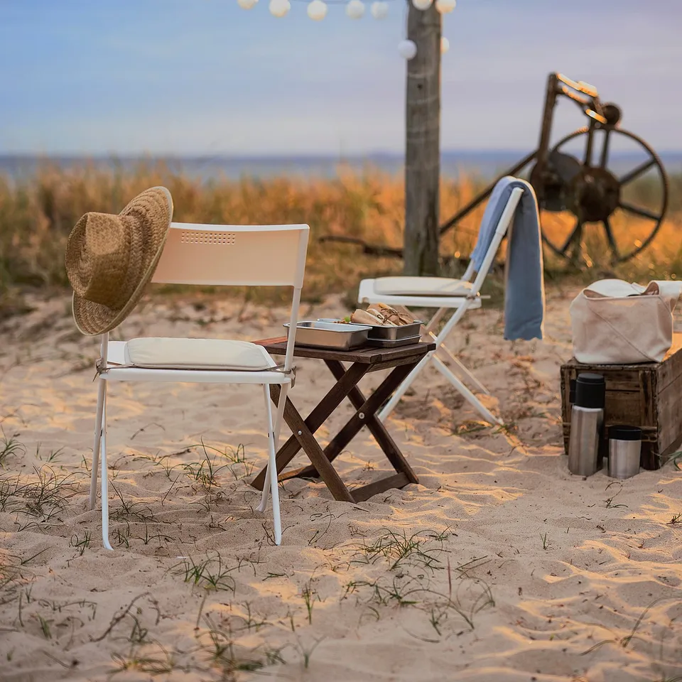 Beach scene with white BRÄMÖN chairs, hat, lights, sand, and wheels.