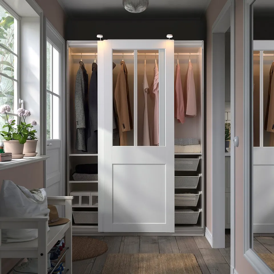 Modern white wardrobe with sliding doors, neat clothes, and green plants.