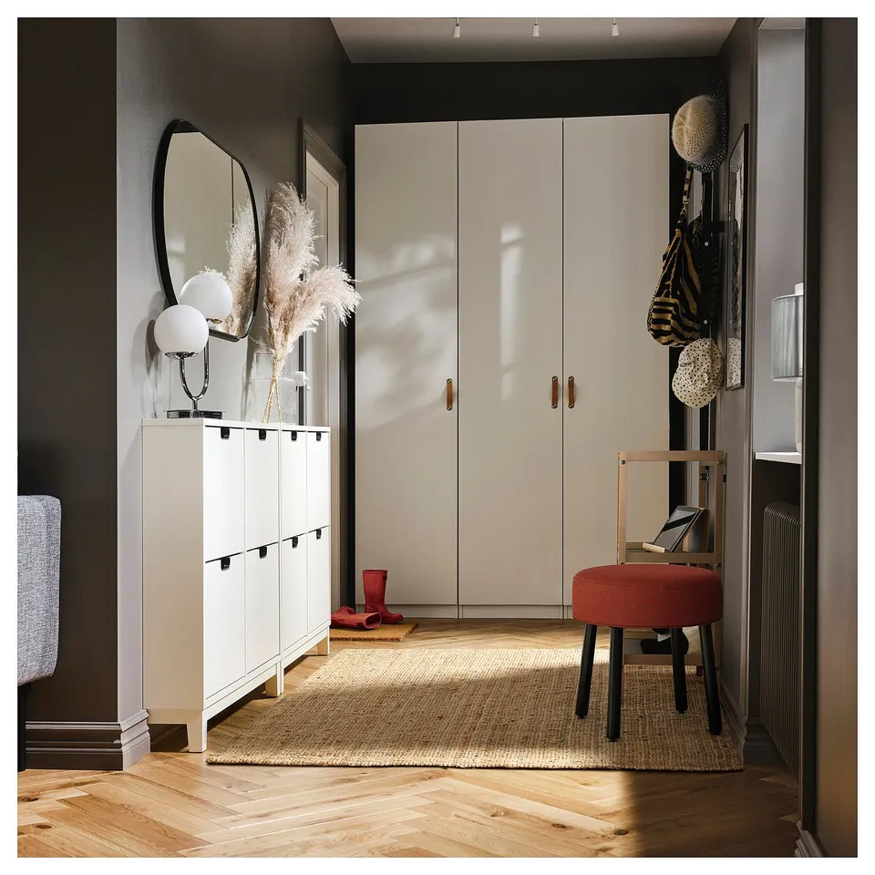 Modern entryway with white cabinets, large mirror, round red stool, jute rug, and wooden floors.