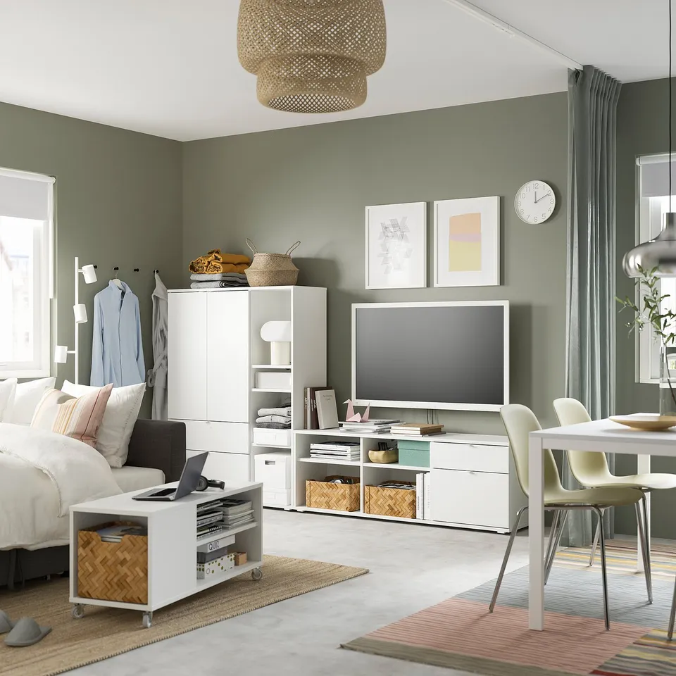 Modern living room with green walls, featuring a white VIHALS tv stand, a cosy bed, and a round rug.