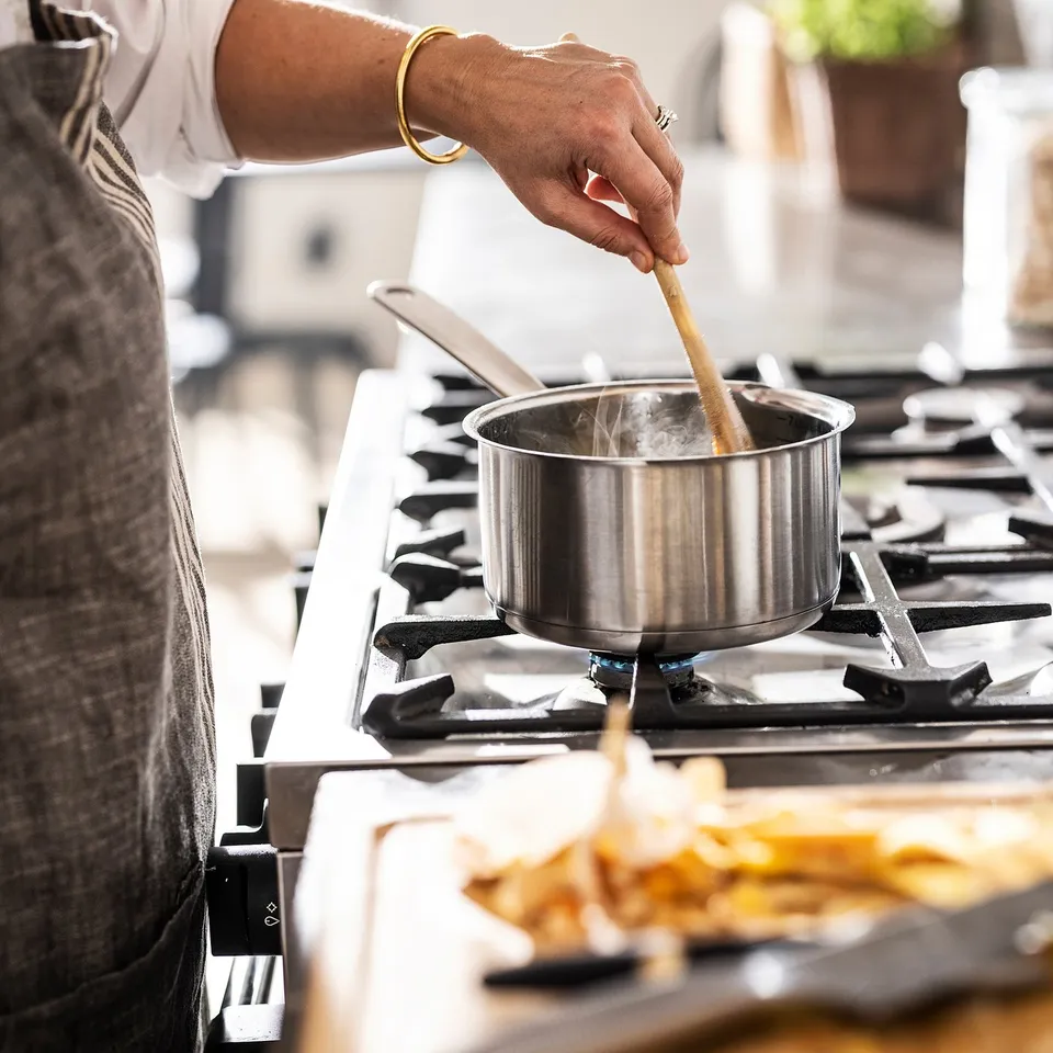 Person stir-frying food on a stove using a metal pan and a wooden spatula.