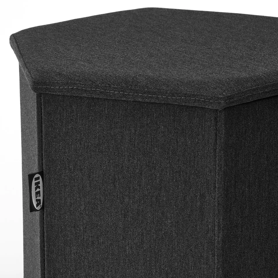 Dark grey fabric-covered storage ottoman with clean stitching and a small IKEA tag.