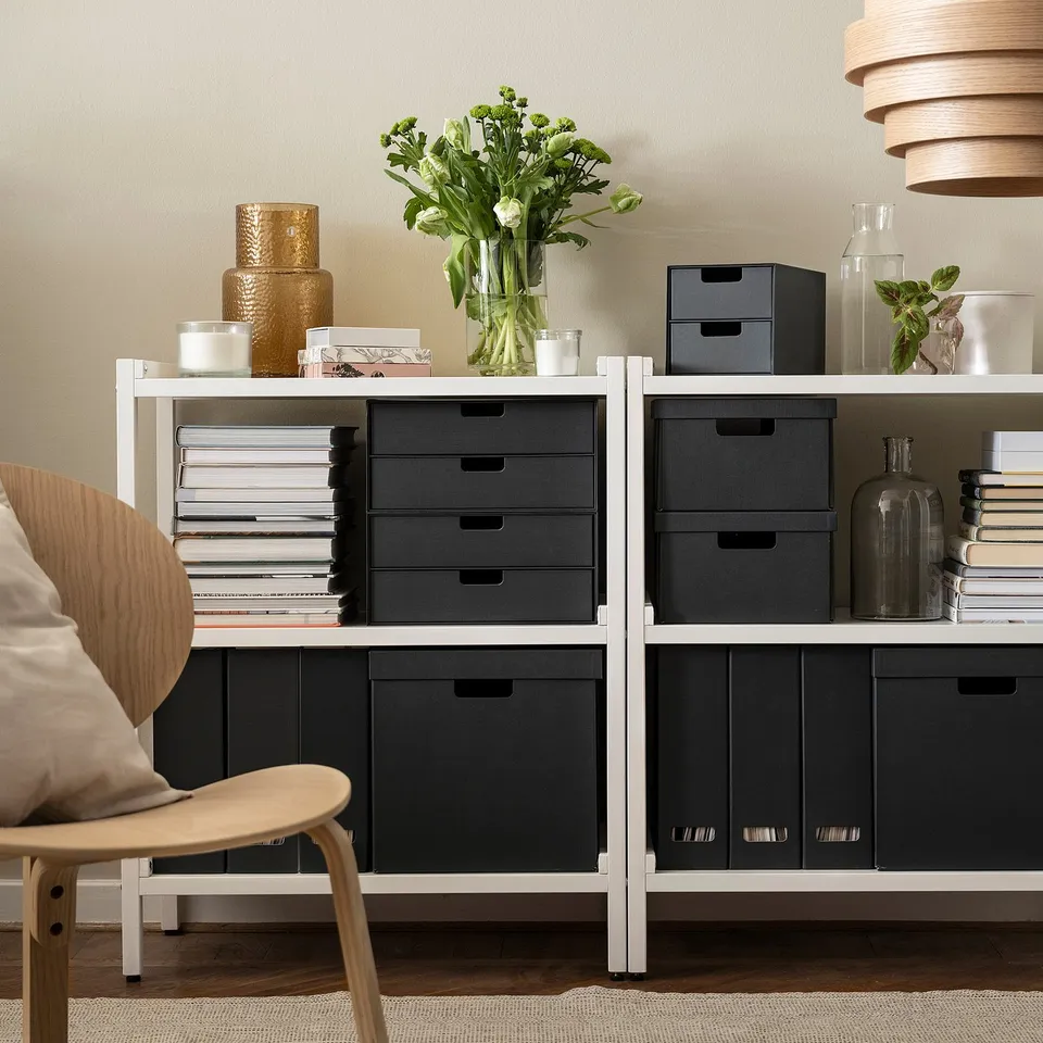 Rectangular storage shelf with black boxes, books, and vase with flowers. Fits neatly against a wall.