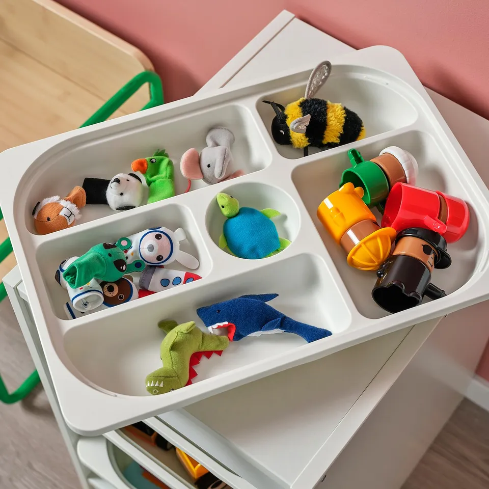 White TROFAST storage tray, divided into six sections, holding various childrens toys and items.