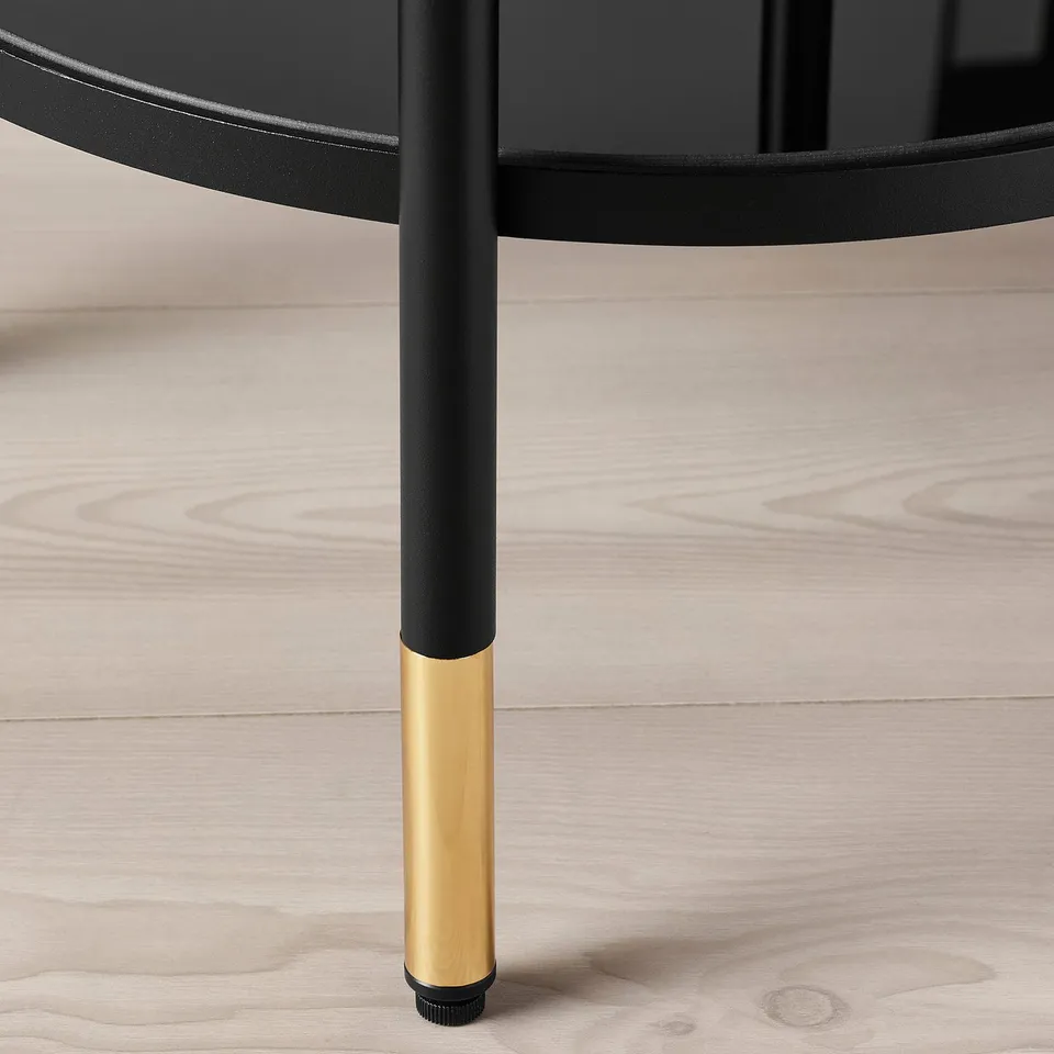 A close-up of a sleek, modern table leg. Black metal with a gold base, on a wooden floor.