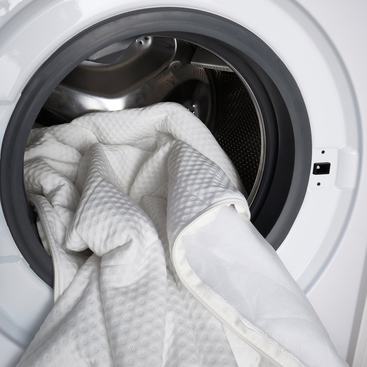 White washing machine filled with large white comforter, showing drums capacity and laundry functionality.