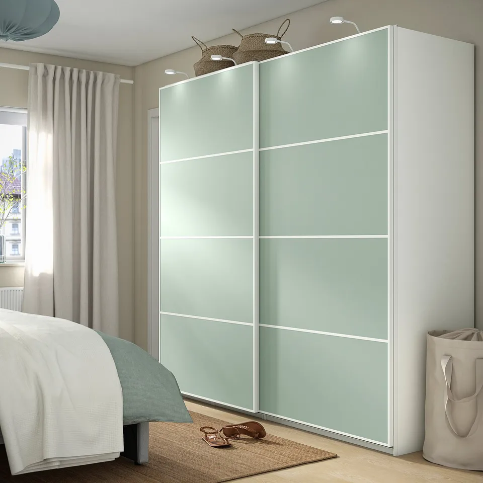 Modern bedroom MEHAMN light blue-green sliding closet, tall & narrow, flanking cosy bed. White curtained window, beige rug & bag beside.