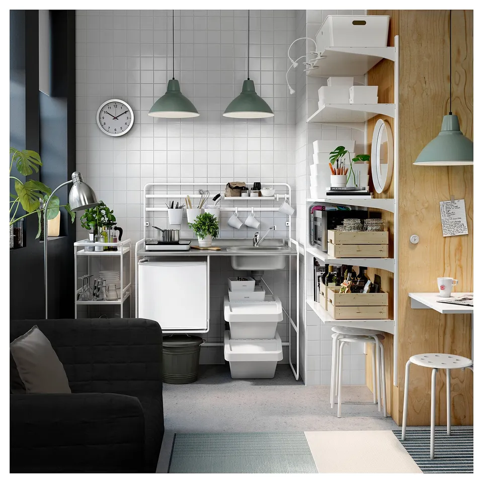 Modern kitchen with SUNNERSTA, white shelves, green pendants, black couch, stainless sink, plants, utensils.