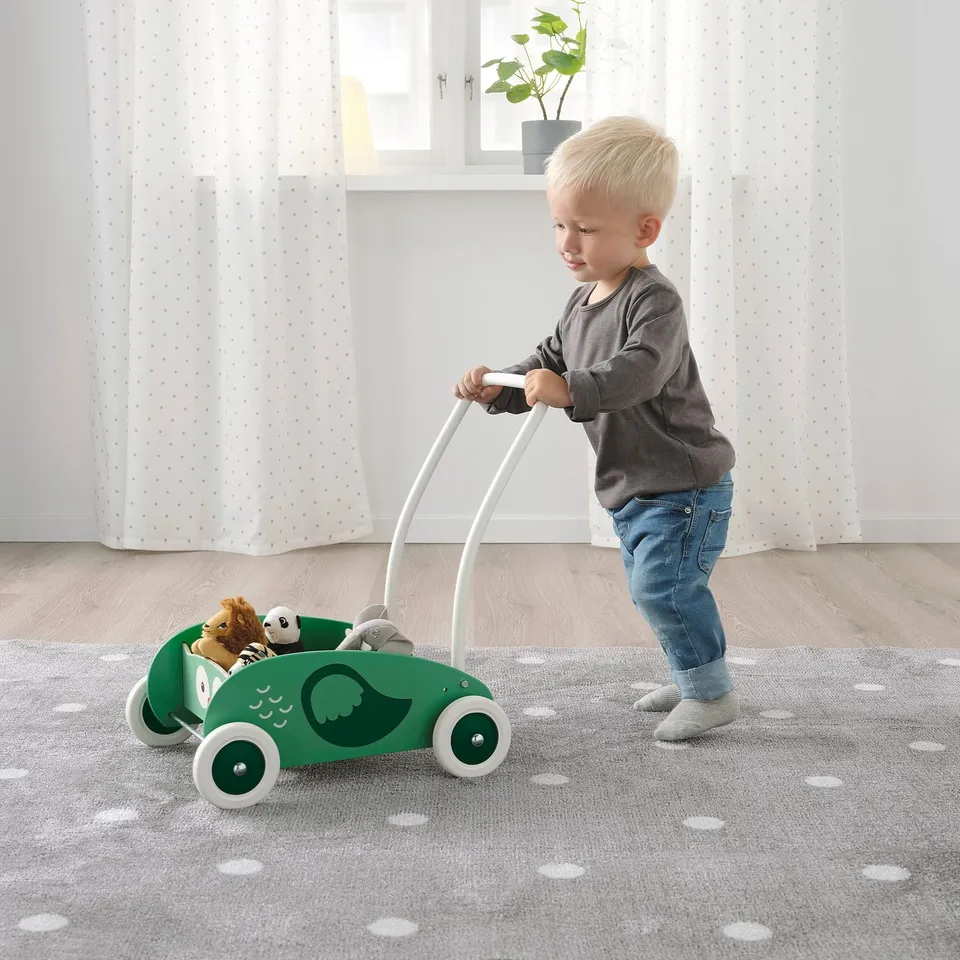 Boy pushes green walker with lion figure.