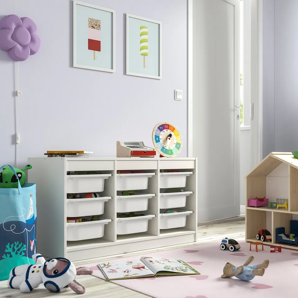 Kids room with TROFAST toy storage, books, dollhouse, and stuffed animals. Bright art and pastel rug.