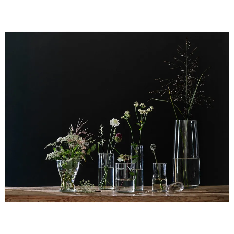 Several glass vases of varying sizes and shapes on a wooden table against a dark background, holding flowers.
