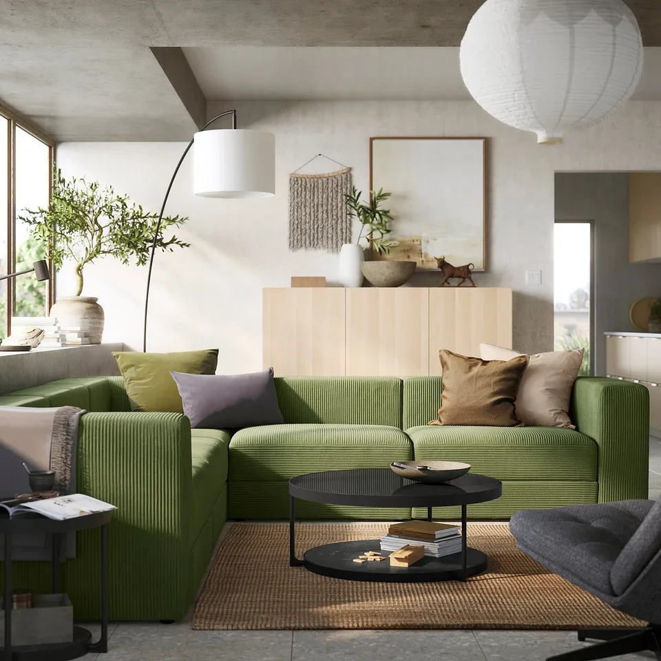 Modern living room with green JÄTTEBO modular sofa, wooden coffee table, large plant, pendant lights, and textured rug.
