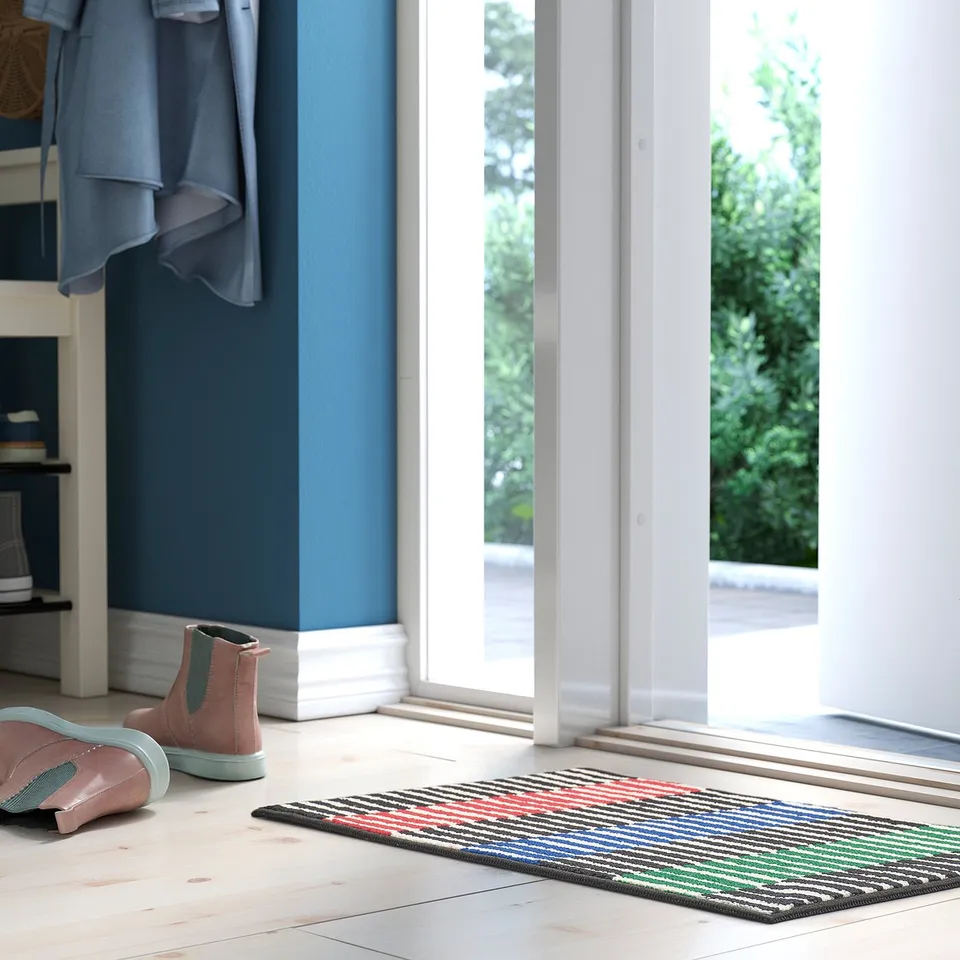 VÄNDPLATS striped mat near entrance door, pink boots, blue wall, white floor.