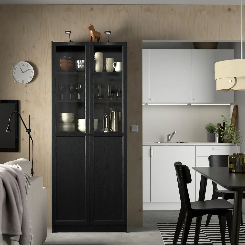 Modern dining with BILLY bookcase, glass doors, kitchen, black table.