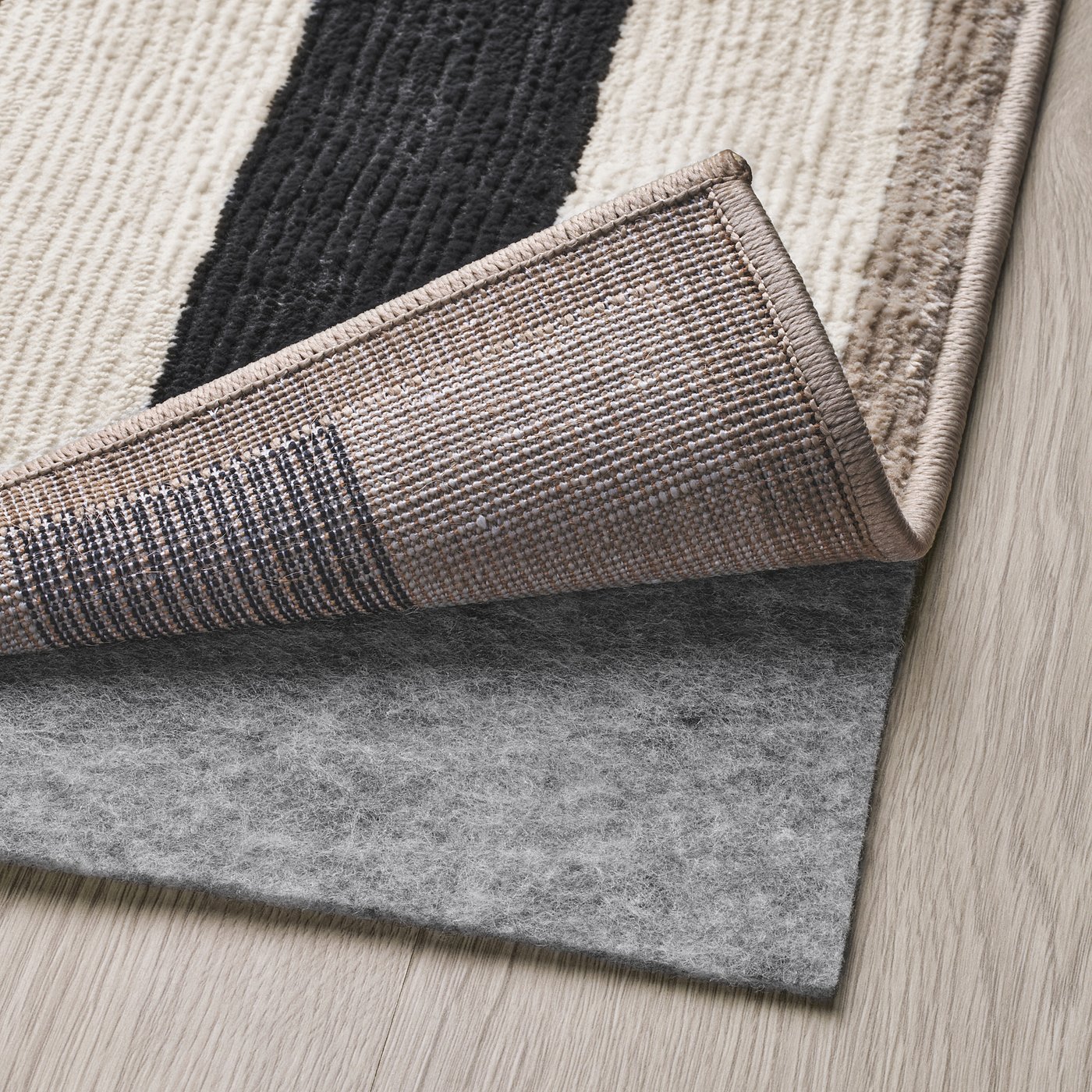 Grey rug with black patches folded, revealing a grey felt underlay, emphasising the rugs soft, low pile and anti-slip functionality.