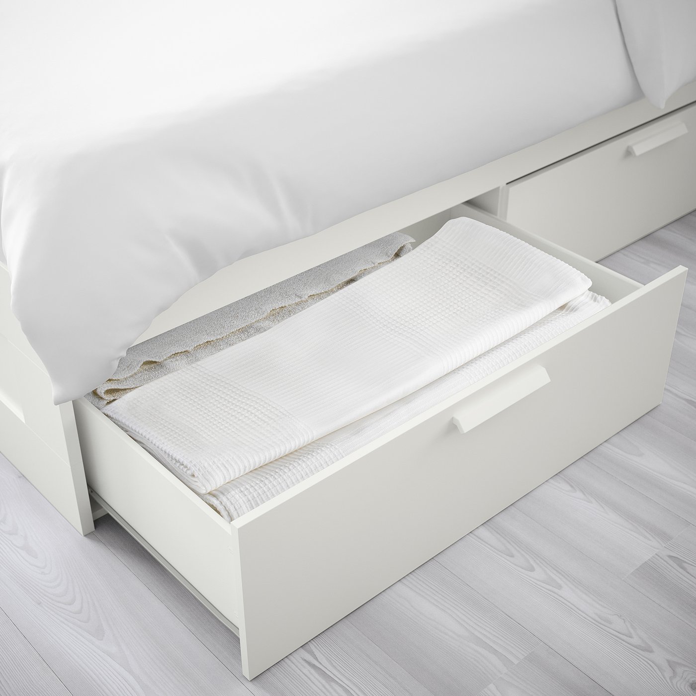 Open white bed storage drawer showing folded textiles. Compact design with under-bed storage for small spaces.
