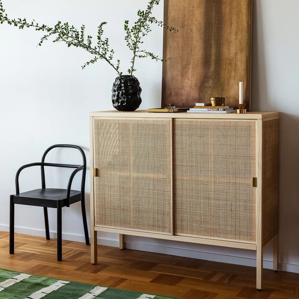 Minimalist room with light wood cabinet, dark chair, & black vase. Steady, tall, slim.