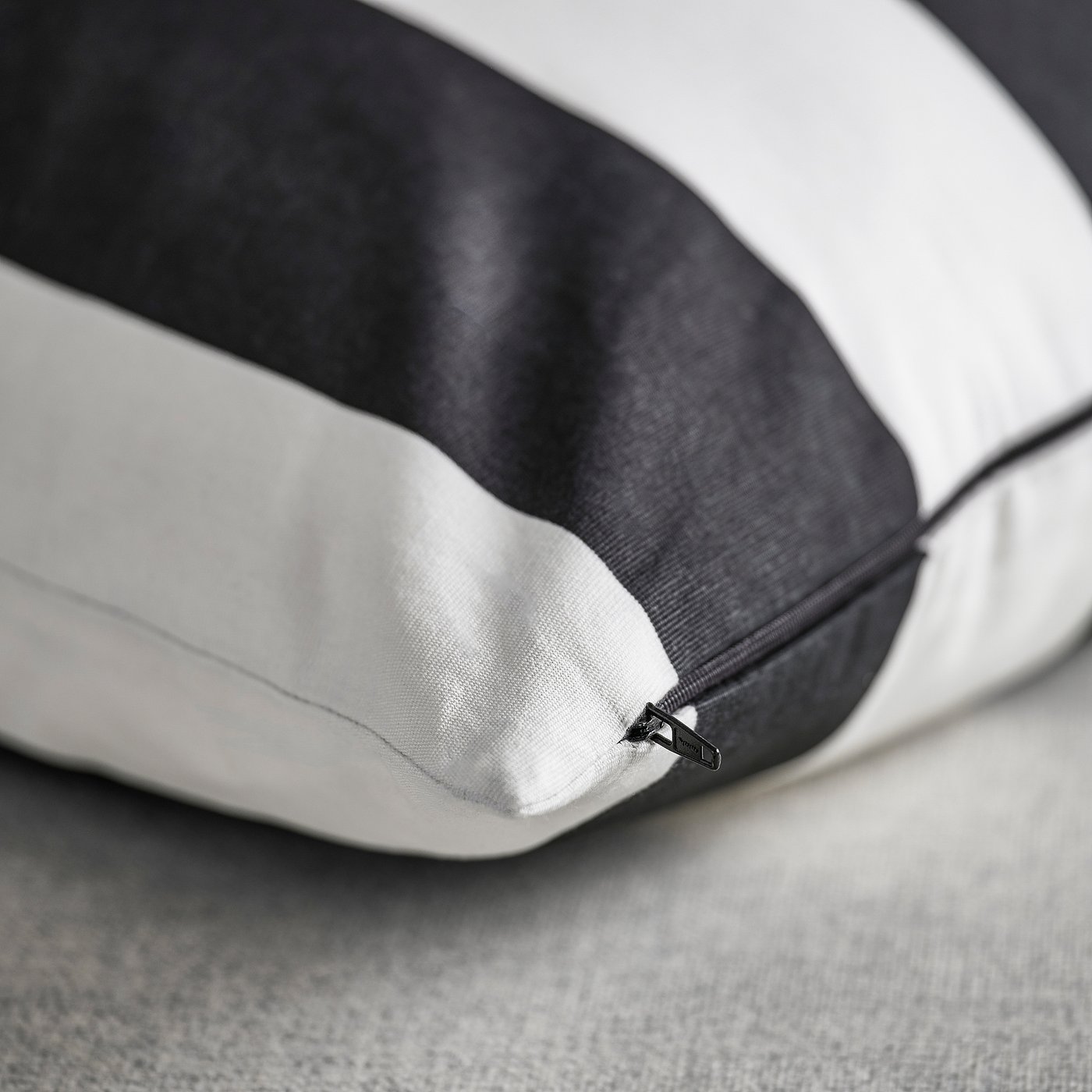 Close-up of a cushion cover with black and white stripes, featuring a hidden zip closure.