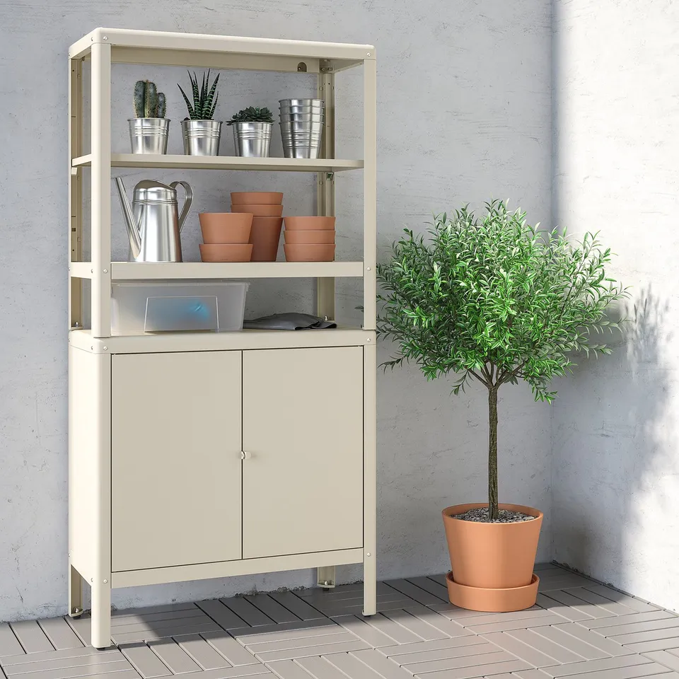Off-white storage unit with open/closed compartments, plants, pots, and tree beside.