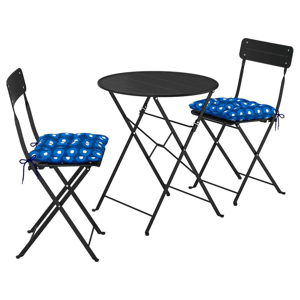 A black SUNDSÖ bistro set with a round table and two foldable chairs, each with a blue circular cushion.