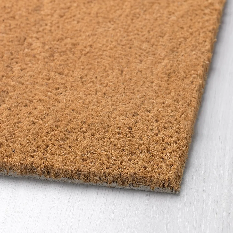 Coir-fiber doormat on light wood, close-up reveal of dense, natural texture.