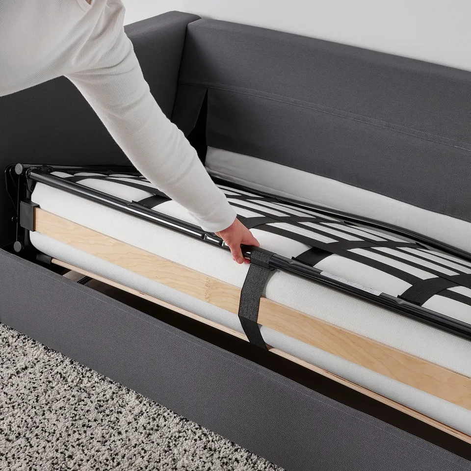 Person adjusts convertible sofa-bed with thick mattress, showcasing its easy transformation and comfort.